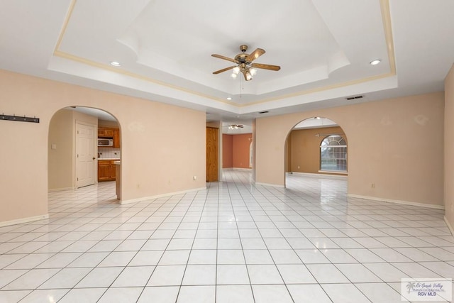 empty room featuring ceiling fan, a tray ceiling, and light tile patterned floors