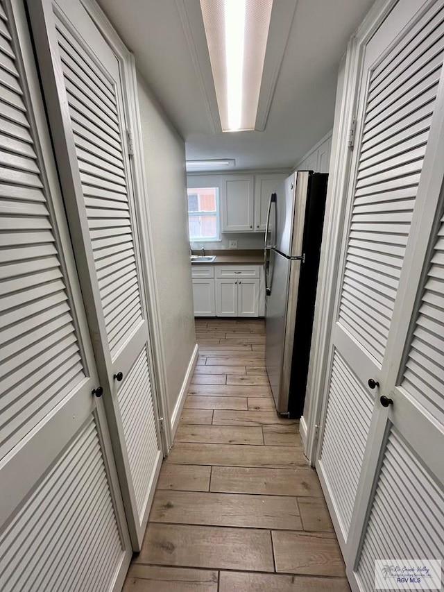 kitchen with stainless steel refrigerator, sink, white cabinets, and light wood-type flooring