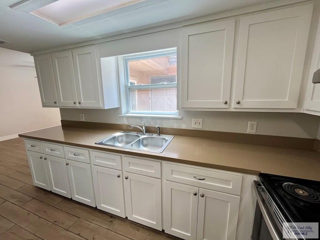 kitchen featuring stainless steel range with electric cooktop, white cabinetry, sink, and light hardwood / wood-style flooring