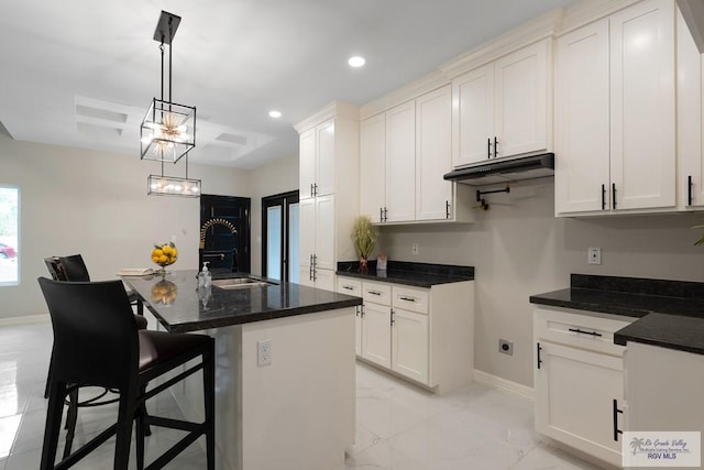 kitchen featuring hanging light fixtures, a kitchen island with sink, white cabinetry, a kitchen breakfast bar, and sink