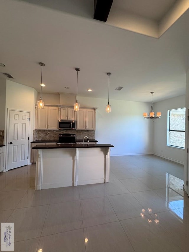 kitchen featuring backsplash, hanging light fixtures, black electric range, an island with sink, and white cabinetry