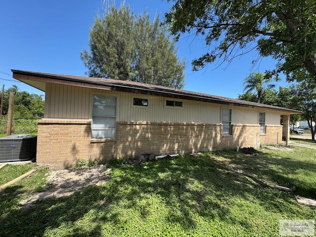 view of property exterior with brick siding, central air condition unit, and a yard