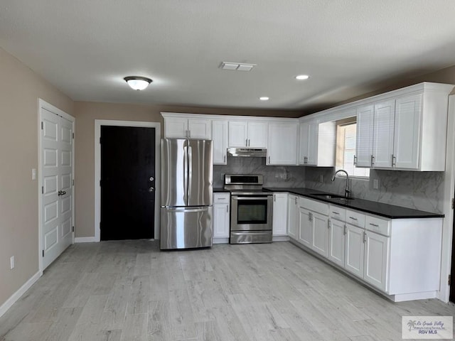 kitchen with stainless steel appliances, a sink, under cabinet range hood, dark countertops, and light wood-style floors
