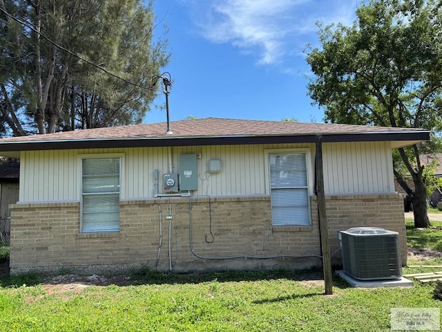 view of home's exterior featuring cooling unit, brick siding, a lawn, and a shingled roof