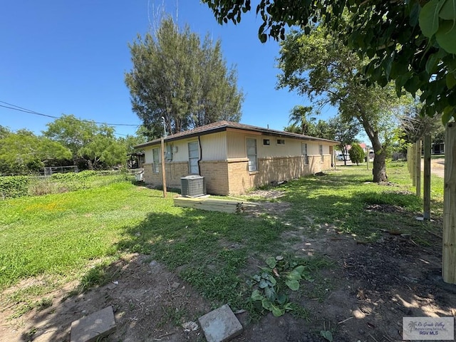 view of side of property with brick siding, a lawn, and central AC unit