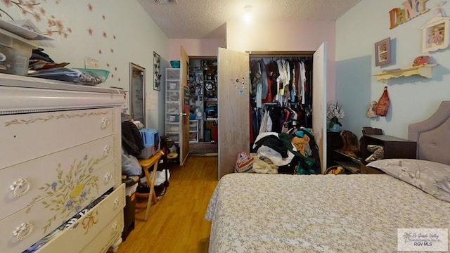 bedroom featuring light wood-style floors, a textured ceiling, visible vents, and a closet