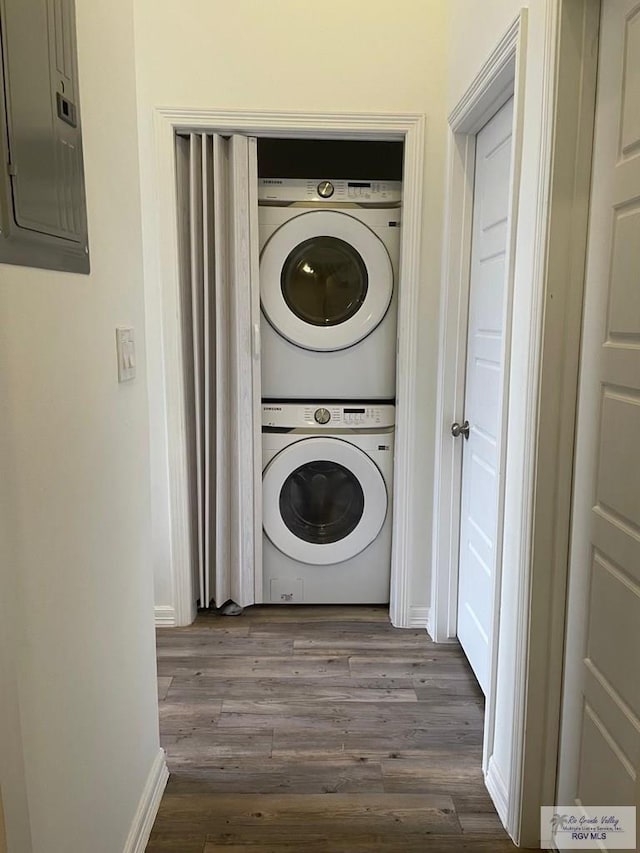 laundry room featuring laundry area, stacked washer and dryer, baseboards, electric panel, and dark wood finished floors