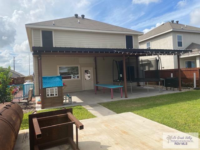 back of property with a trampoline, a patio area, and a lawn