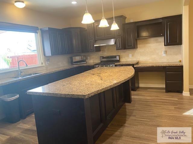 kitchen featuring ventilation hood, hanging light fixtures, stainless steel stove, light hardwood / wood-style flooring, and a kitchen island