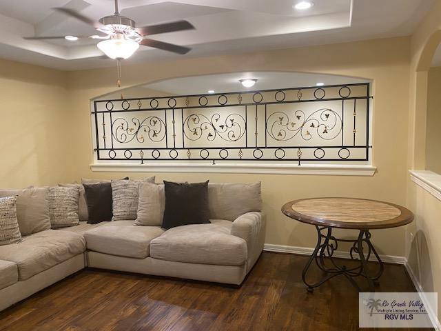 living room featuring a raised ceiling, ceiling fan, and dark hardwood / wood-style flooring