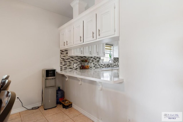 kitchen featuring a breakfast bar, backsplash, white cabinets, light countertops, and light tile patterned floors