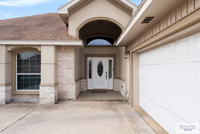 doorway to property with visible vents, stucco siding, stone siding, a shingled roof, and brick siding