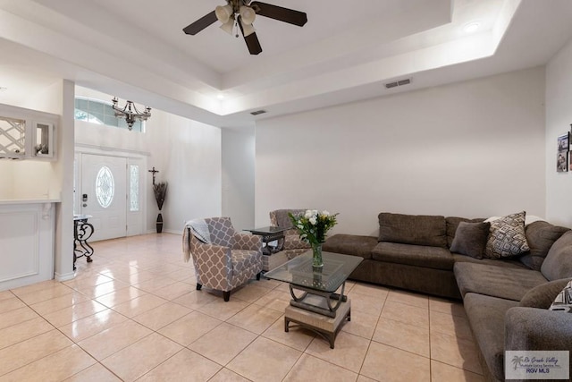 living area featuring a raised ceiling, light tile patterned floors, ceiling fan with notable chandelier, and visible vents