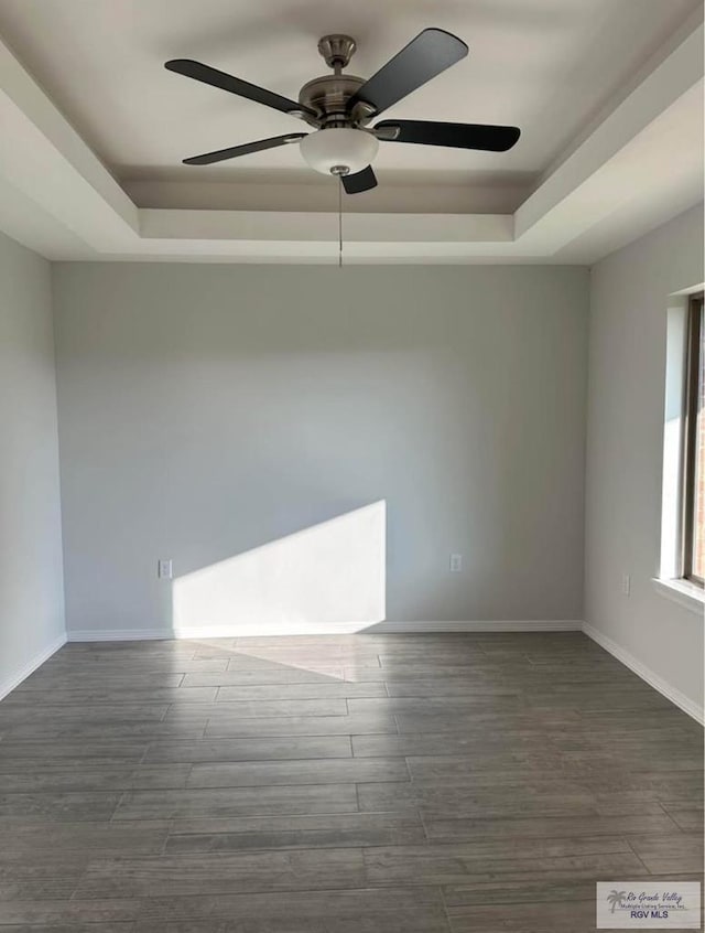 unfurnished room with a raised ceiling, ceiling fan, and dark hardwood / wood-style flooring