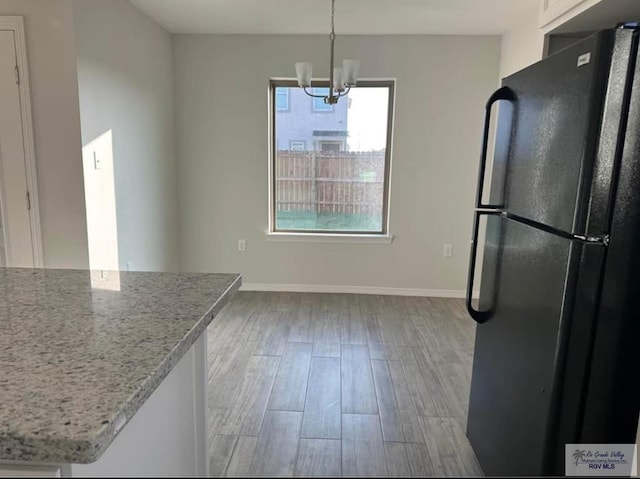 kitchen featuring hanging light fixtures, black fridge, light stone countertops, an inviting chandelier, and light hardwood / wood-style flooring