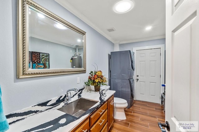 bathroom with vanity, wood finish floors, stacked washer and clothes dryer, crown molding, and toilet