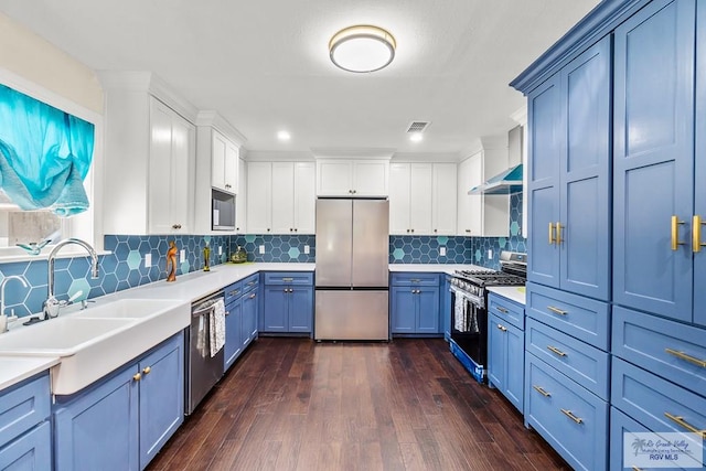 kitchen featuring blue cabinets, a sink, wall chimney range hood, stainless steel appliances, and light countertops