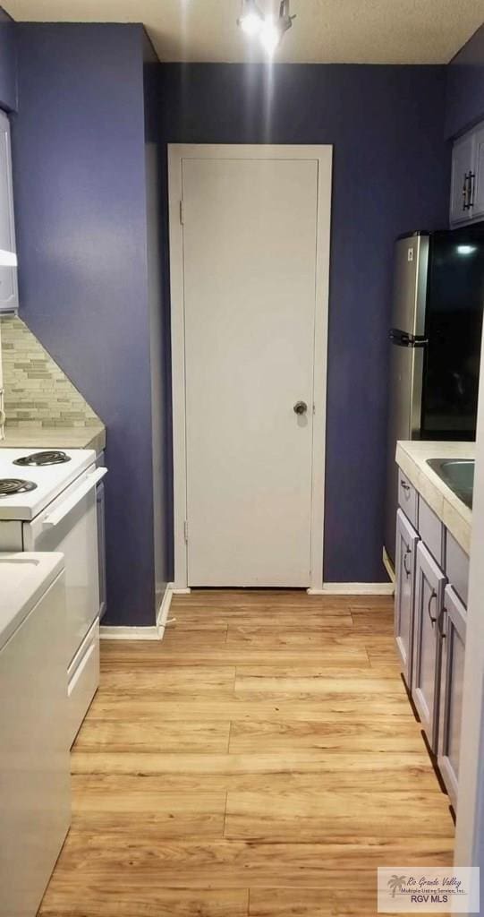 kitchen featuring decorative backsplash, stainless steel fridge, light hardwood / wood-style floors, and white range with electric stovetop
