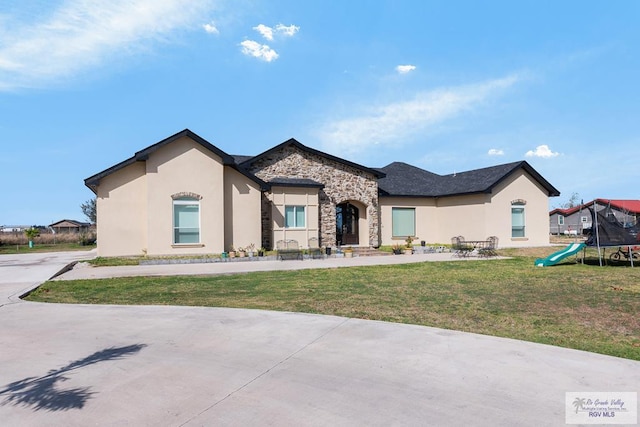 view of front of house featuring stone siding, a trampoline, a front lawn, and stucco siding