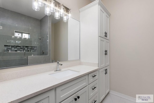 bathroom featuring marble finish floor, a tile shower, vanity, and baseboards