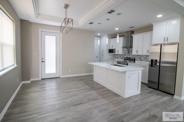 kitchen with appliances with stainless steel finishes, sink, wall chimney range hood, pendant lighting, and white cabinetry