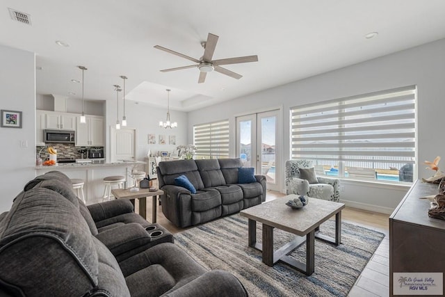 living room with ceiling fan with notable chandelier, a wealth of natural light, light hardwood / wood-style floors, and a raised ceiling