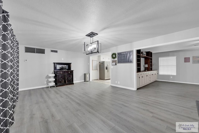 unfurnished living room featuring light hardwood / wood-style floors, a textured ceiling, and a notable chandelier