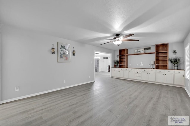 unfurnished living room with a healthy amount of sunlight, ceiling fan with notable chandelier, light hardwood / wood-style flooring, and a textured ceiling