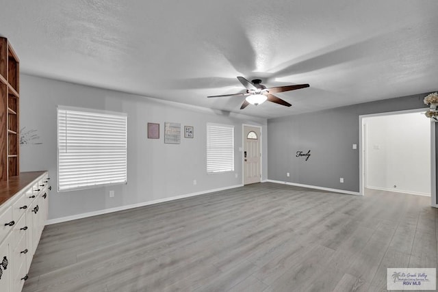 unfurnished living room with a textured ceiling, light hardwood / wood-style flooring, and ceiling fan