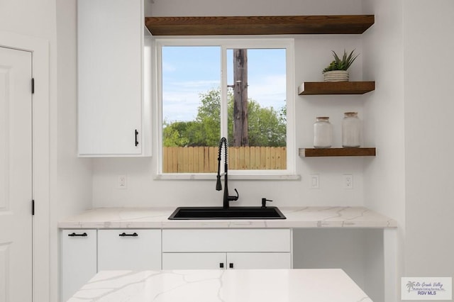 kitchen featuring a sink, open shelves, light stone countertops, and white cabinets