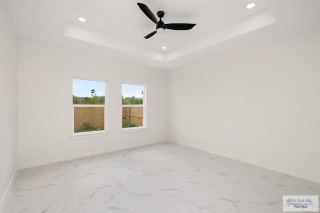 empty room featuring recessed lighting, a tray ceiling, marble finish floor, and a ceiling fan