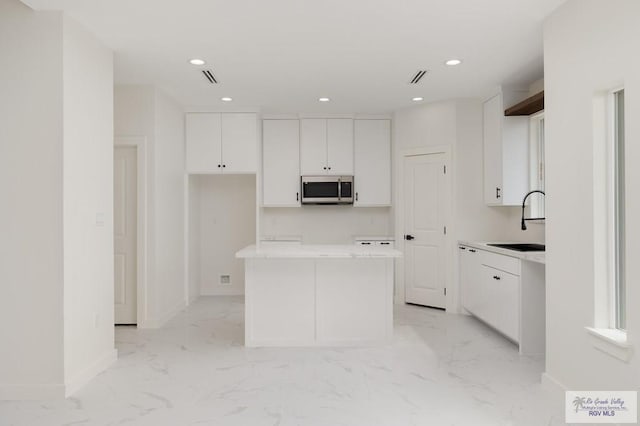 kitchen featuring stainless steel microwave, a kitchen island, white cabinets, marble finish floor, and a sink