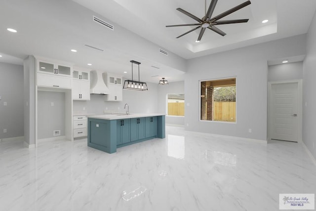 kitchen with premium range hood, blue cabinets, white cabinetry, an island with sink, and pendant lighting