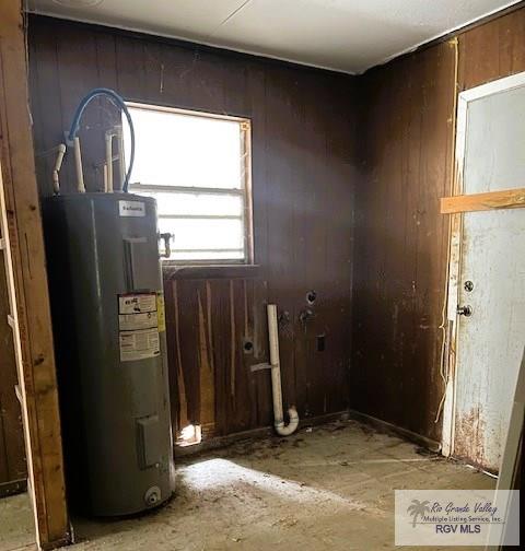 misc room featuring electric water heater and wood walls