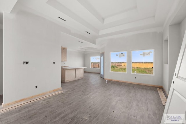 interior space featuring a towering ceiling, light wood-style flooring, baseboards, and a raised ceiling