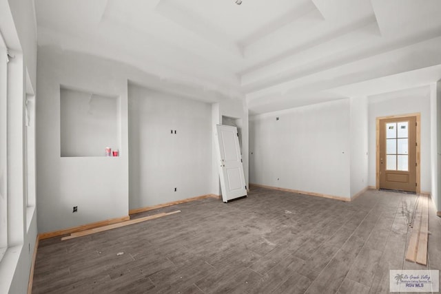 spare room with a tray ceiling, wood finished floors, and baseboards