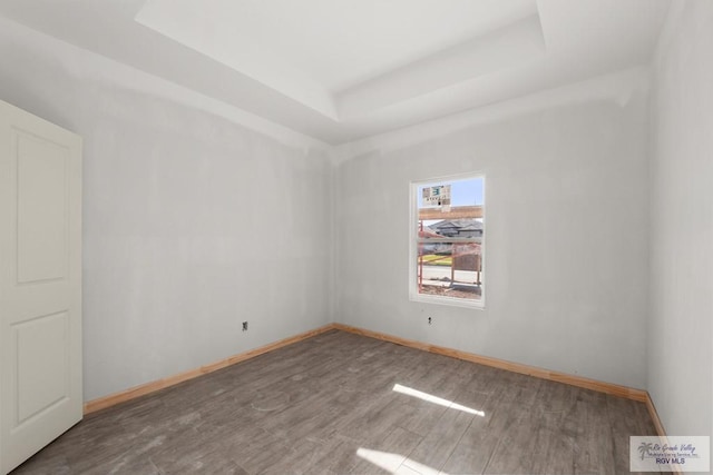 spare room featuring a tray ceiling, wood finished floors, and baseboards