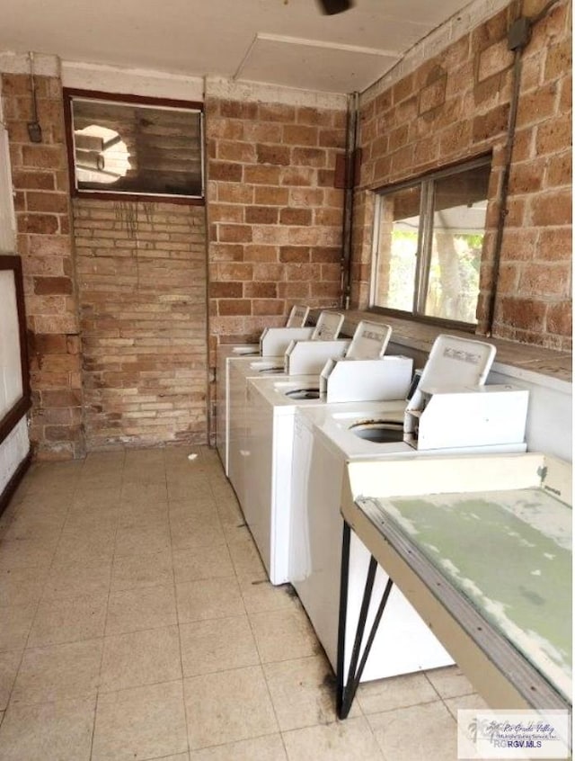 clothes washing area with washer and dryer and brick wall