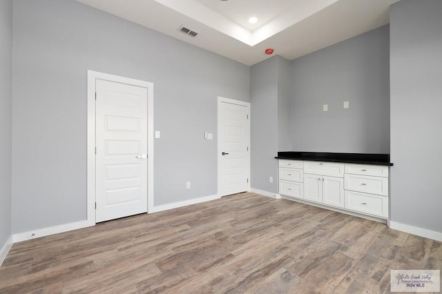 unfurnished bedroom featuring a raised ceiling, visible vents, baseboards, recessed lighting, and light wood finished floors