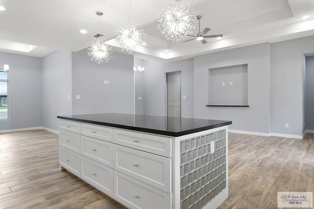 kitchen with light wood-type flooring, dark countertops, and a tray ceiling