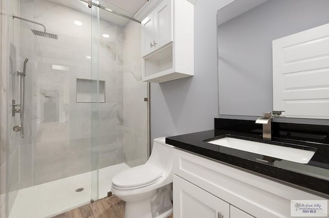 bathroom featuring wood finished floors, a shower stall, toilet, and vanity