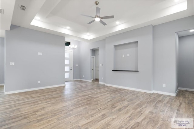 unfurnished living room with light wood-style flooring, visible vents, a tray ceiling, and ceiling fan with notable chandelier