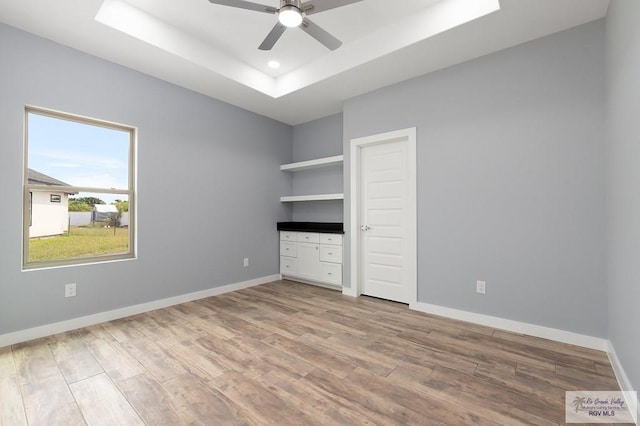 unfurnished bedroom with light wood-type flooring, baseboards, and a tray ceiling