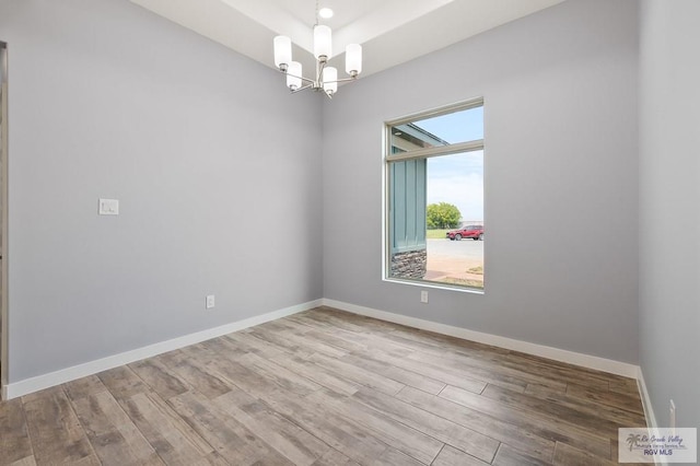 unfurnished room featuring a chandelier, baseboards, and wood finished floors