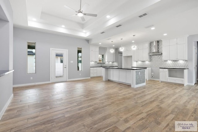 kitchen featuring wall chimney exhaust hood, a ceiling fan, visible vents, and backsplash
