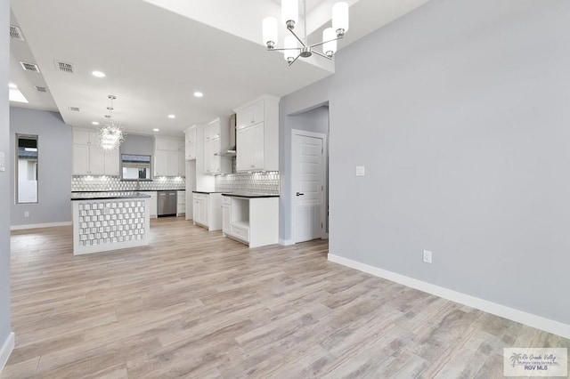 kitchen with an inviting chandelier, wall chimney exhaust hood, visible vents, dark countertops, and dishwasher