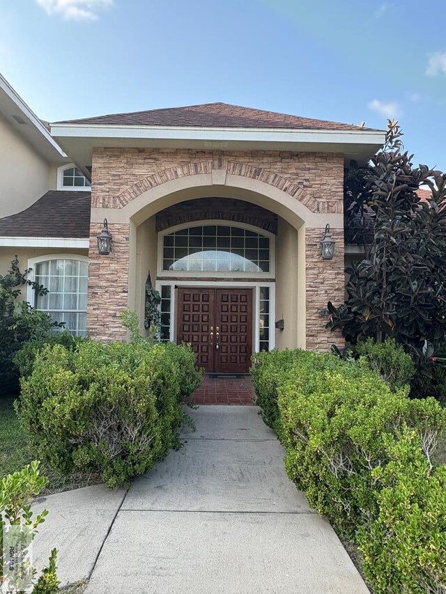 901 Plantation St, Brownsville, TX 78526 - view of exterior entry featuring stone siding, stucco siding, and roof with shingles
