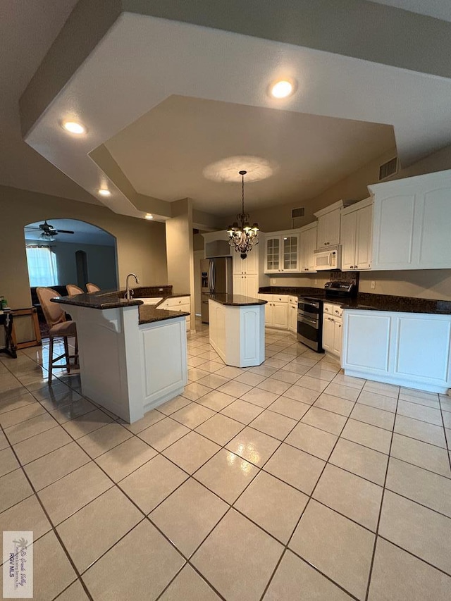 901 Plantation St, Brownsville, TX 78526 - kitchen featuring white microwave, stainless steel range, dark countertops, a center island, and light tile patterned floors