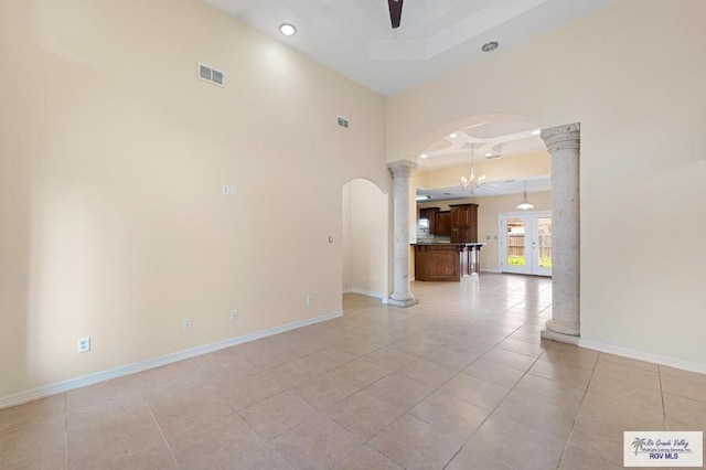 unfurnished room featuring a raised ceiling, a towering ceiling, light tile patterned floors, ceiling fan with notable chandelier, and ornate columns