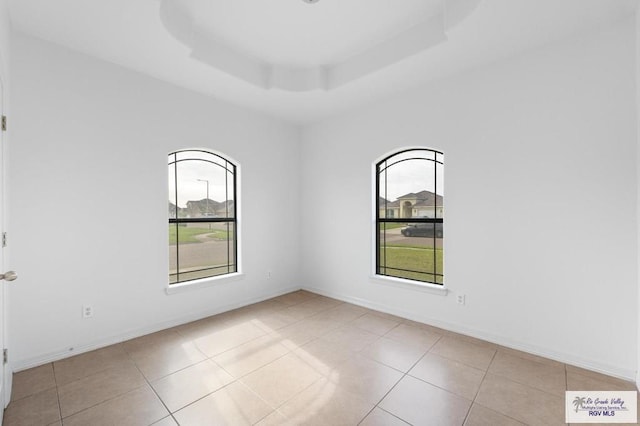 tiled empty room featuring a tray ceiling